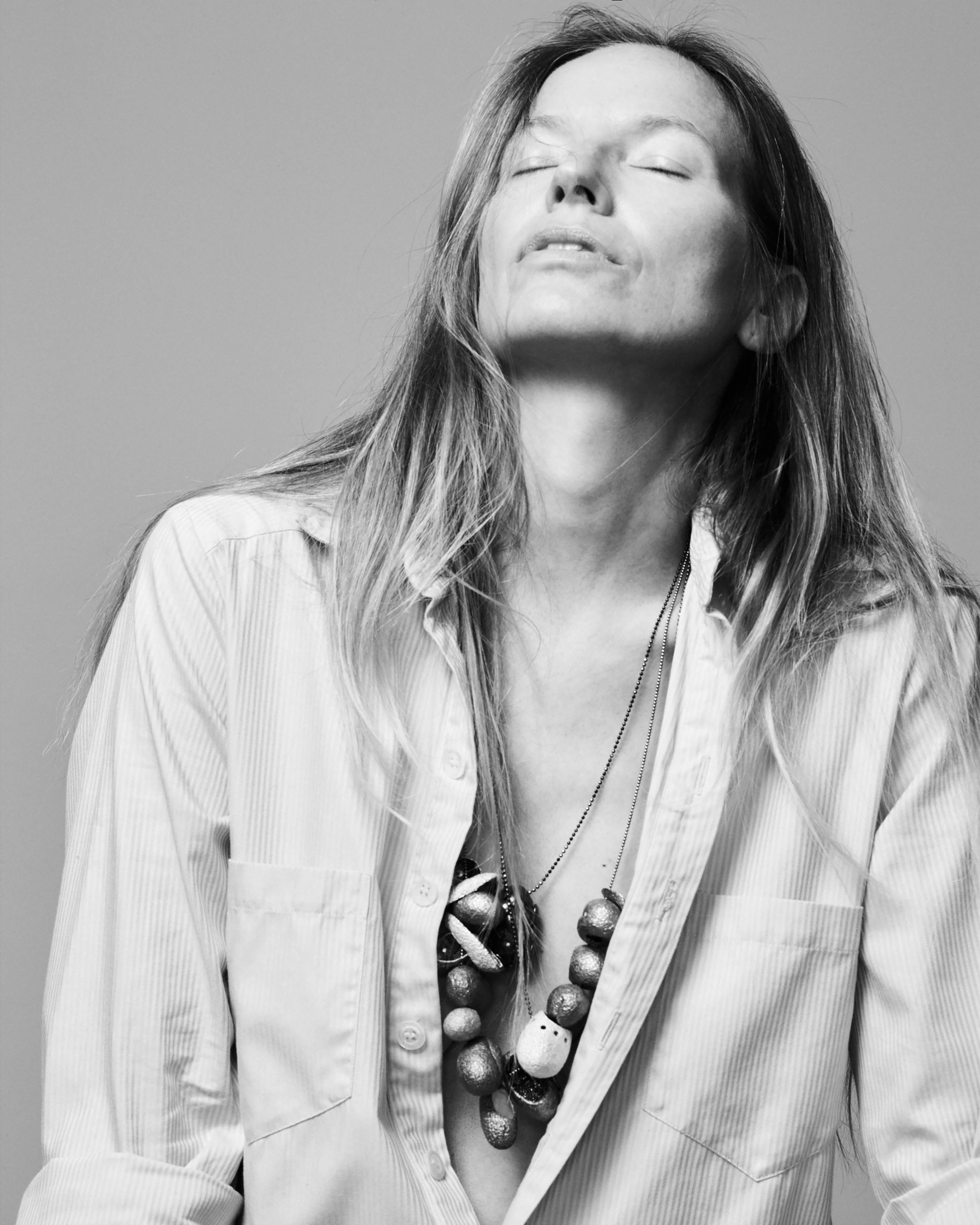 Künstlerin Michaela Schwarz–Weismann trägt viele Seidenkokon–Ketten über einem hellen Hemd, sie hat den Kopf nach hinten gelegt, ihre Augen sind geschlossen